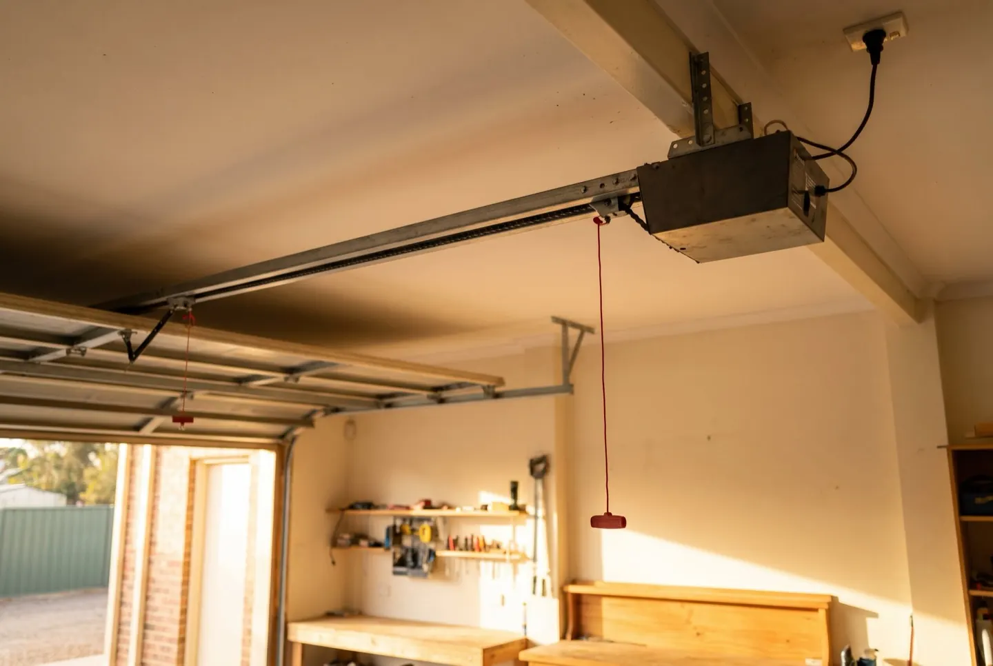 A ceiling-mounted garage door opener and drive rail with its red manual release cord hanging down
